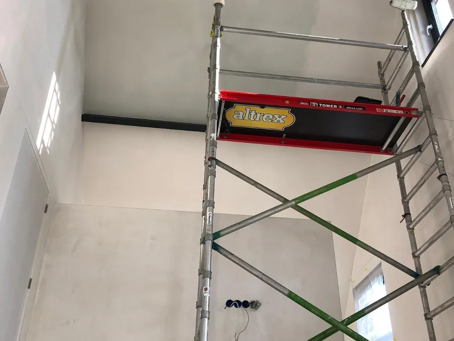 Hoge woonkamer in aanbouw met een rolsteiger tegen de gesausde wand