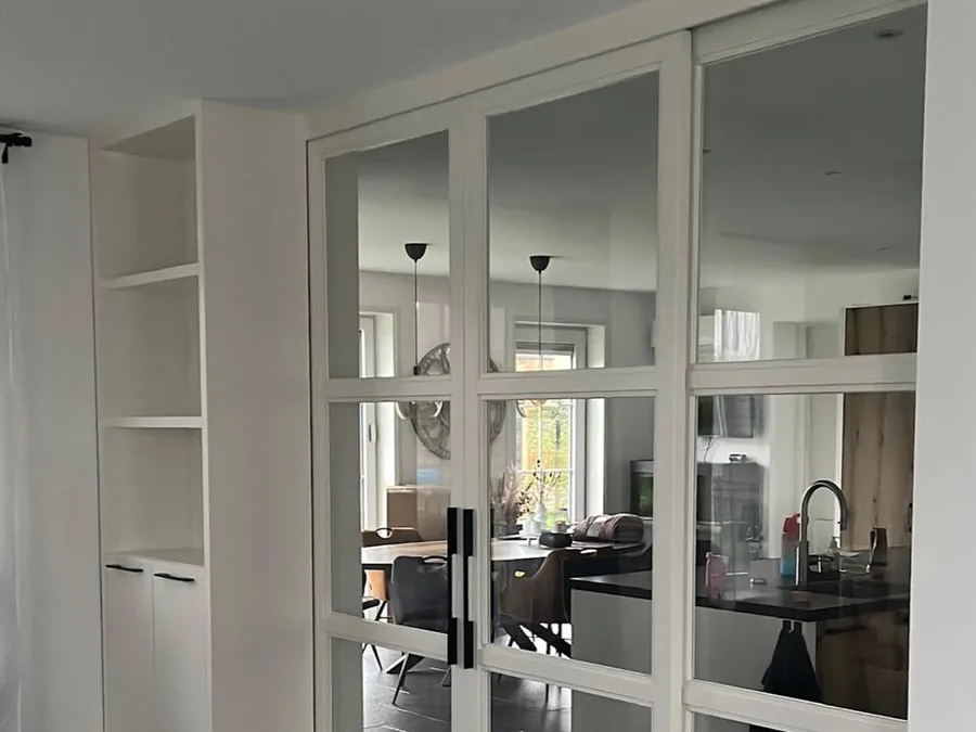 Woonkamer met witgelakte taatsdeuren met glasvlakken naar de keuken